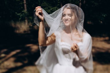 Gelinlik ve duvak takmış, dışarıda poz veren güzel mutlu genç gelinin portresi           