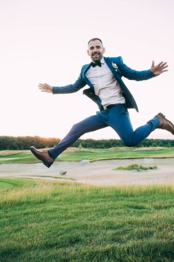 Yakışıklı, mutlu genç damat gün batımında parkta zıplıyor.       