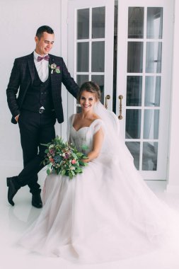 Güzel genç gelin ve yakışıklı damat düğün iç mekanında birlikte poz veriyorlar.            