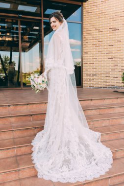 Güzel, mutlu, genç bir gelinin portresi basamaklarda poz veriyor.