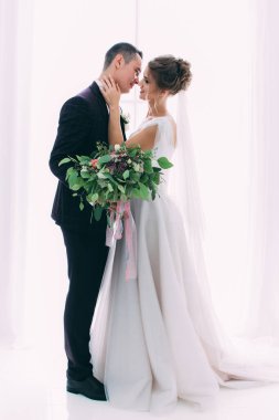 Mutlu ve şık gelin ve damat düğün salonunda buketle                   