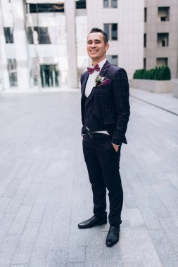 Takım elbiseli yakışıklı, papyonlu, şehirde gülümseyen genç damat.