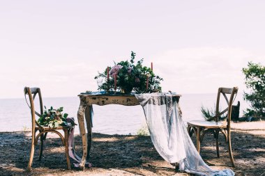 Çiçekli düğün masası, mumlar ve plajdaki sandalyeler.