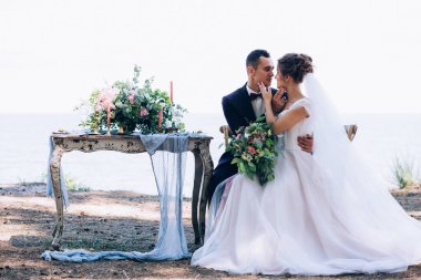 Güzel bir düğün çifti sahildeki masada poz veriyor. Gelin ve damat düğün gününde.                      