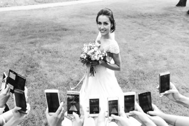 Akıllı telefonlar tutan ve güzel genç gelinlerin fotoğraflarını çeken insanların siyah beyaz görüntüleri.