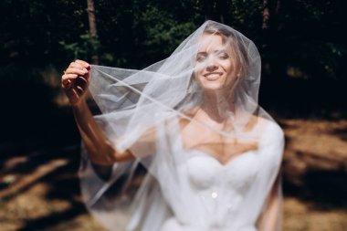 Gelinlik ve duvak takmış, dışarıda poz veren güzel mutlu genç gelinin portresi           