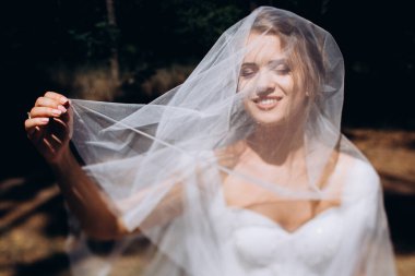 Gelinlik ve duvak takmış, dışarıda poz veren güzel mutlu genç gelinin portresi           