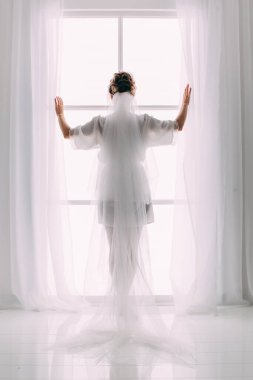 Pencere kenarında poz veren beyaz peçeli güzel gelinin arka manzarası          