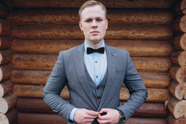 Ahşap duvarda duran takım elbiseli yakışıklı damadın portresi.             