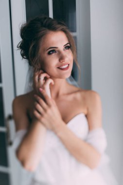 Beyaz elbiseli ve duvaklı güzel gelinin portresi düğün sabahı poz veriyor.            