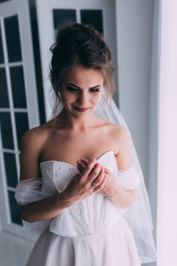 Beyaz elbiseli ve duvaklı güzel gelinin portresi düğün sabahı poz veriyor.            