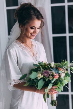 Genç, mutlu gelin ve bir buket çiçekle düğün içinde poz veriyor.         