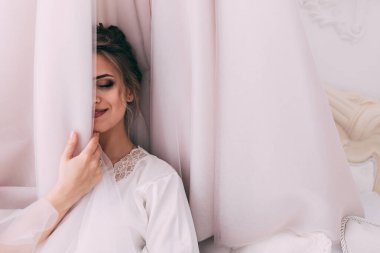 Güzel, mutlu, genç bir gelin yatak odasında gelinlikle poz veriyor. Gelinin özel sabahı..                     