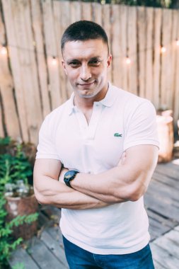 Kollarını kavuşturup kameraya gülümseyen yakışıklı bir gencin portresi. 