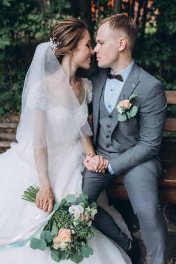 Mutlu gelin ve damat parktaki ahşap bankta oturuyor. 