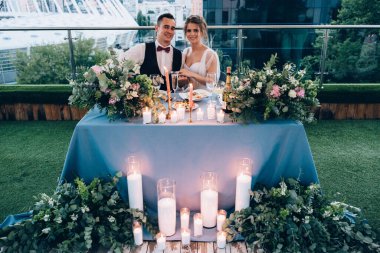 Mutlu gelin ve damat çiçekler ve mumlarla masada.