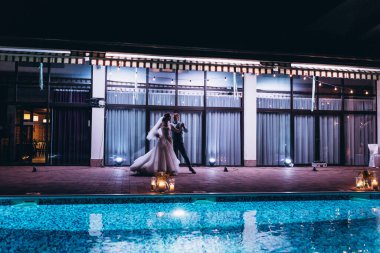 Güzel mutlu gelin ve damat gece yüzme havuzunun yanında dans ediyor.         