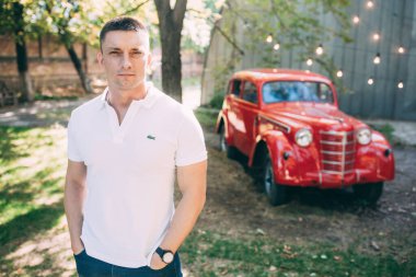 Kırmızı retro arabanın yanında poz veren yakışıklı bir gencin portresi.            