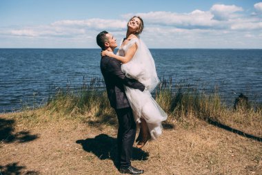 Mutlu gelin ve damat göl kıyısında yürüyorlar.