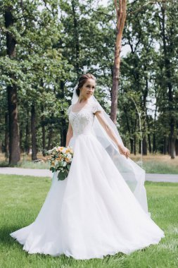 Parkta buketi olan beyaz gelinlik içindeki güzel gelinin portresi.                        