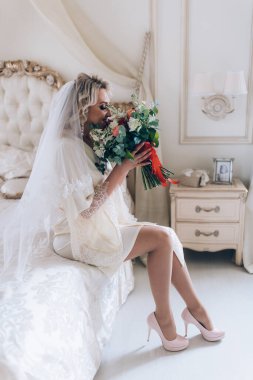 Çiçek buketi tutan ve yatakta oturan güzel gelinin portresi. 