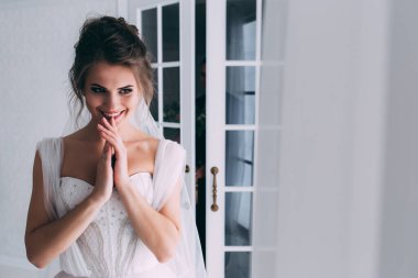 Beyaz elbiseli ve duvaklı güzel gelinin portresi düğün sabahı poz veriyor.            