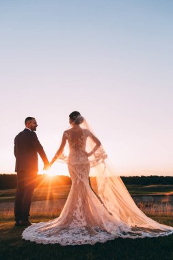 Mutlu gelin ve damat çifti güneş batarken yaz parkında poz veriyor.       