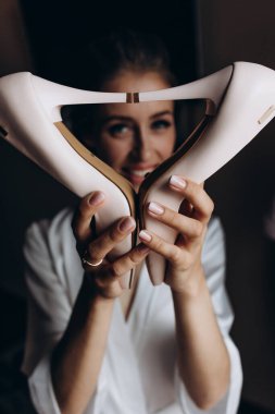 Düğün ayakkabılarıyla poz veren ve kameraya gülümseyen genç bir gelin.  