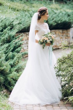 Parkta buketi olan beyaz gelinlik içindeki güzel gelinin portresi.                        