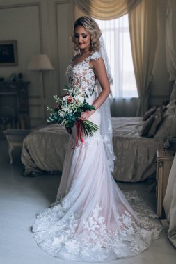 Beyaz elbiseli güzel sarışın gelin lüks içinde düğün buketi ile poz veriyor.              