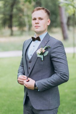 Parkta duran yakışıklı, şık genç damadın portresi.       