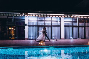 Güzel mutlu gelin ve damat gece yüzme havuzunun yanında dans ediyor.         
