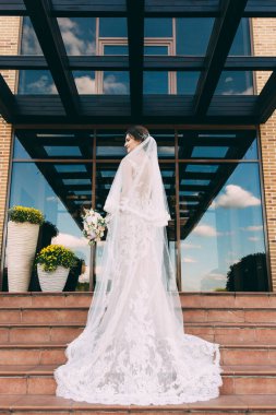 Düğün günü merdivenlerde duran güzel peçeli genç gelinin arka manzarası.