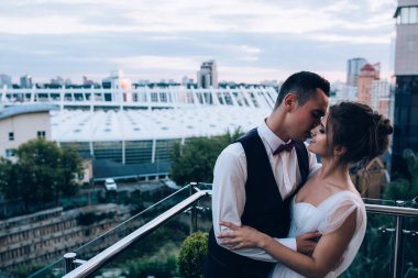 Genç bir çift gelin ve damat şehrin arka planında balkonda poz veriyorlar.     