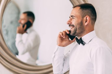 Beyaz gömlekli mutlu genç damat telefonla konuşuyor.      