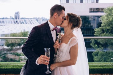 Güzel, mutlu gelin ve damat ellerinde kadehlerle dışarıda şarap içiyorlar.      