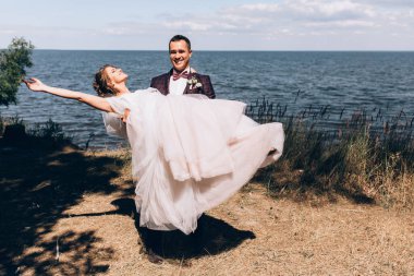 Genç mutlu gelin ve yakışıklı damat sahilde poz veriyor.