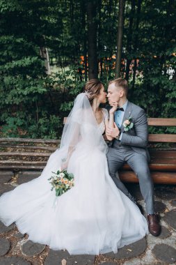 Güzel gelin ve damat parktaki ahşap bankta oturuyor.   