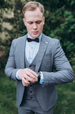 Takım elbiseli yakışıklı genç adam ve dışarıdaki kol saatini kontrol ediyor.       