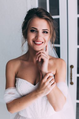 Beyaz elbiseli ve duvaklı güzel gelinin portresi düğün sabahı poz veriyor.            