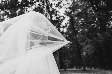 Beyaz gelinlikli güzel gelin ve duvak parkta damatla poz veriyor.