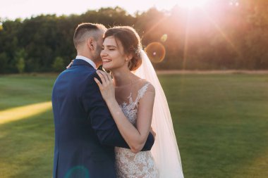 Mutlu gelin ve damat çifti güneş batarken yaz parkında poz veriyor.       