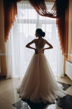 Gelinlik içinde pencerenin yanında duran güzel gelinin arka manzarası.