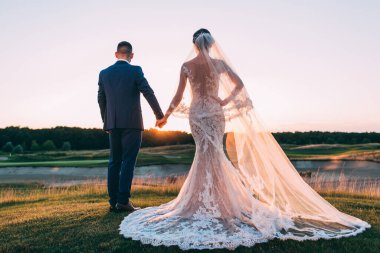 Mutlu gelin ve damat çifti güneş batarken yaz parkında poz veriyor.       