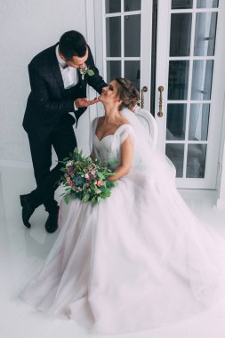 Güzel genç gelin ve yakışıklı damat düğün iç mekanında birlikte poz veriyorlar.            