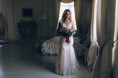 Beyaz elbiseli güzel sarışın gelin lüks içinde düğün buketi ile poz veriyor.              