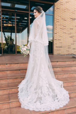 Gelin beyaz elbiseli, elinde düğün buketi basamaklarda duruyor.