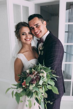 Güzel genç gelin ve yakışıklı damat düğün iç mekanında birlikte poz veriyorlar.            