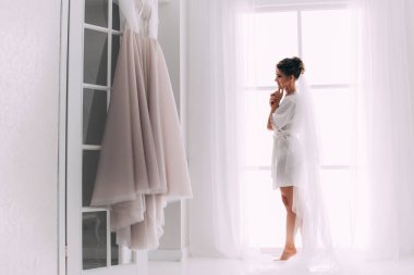 Evde beyaz gelinlikle poz veren güzel mutlu genç gelinin portresi.        