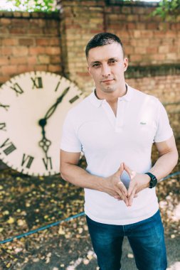 Beyaz gömlekli bir adam dışarıda saat başı poz veriyor. 
